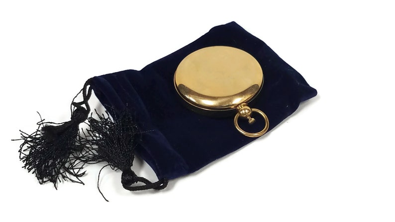 May include: A gold compass with a blue velvet pouch and a black tassel.