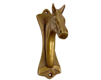 Op de afbeelding: Een gouden messing deurklopper in de vorm van een paardenkop met een decoratieve achterplaat. Het paardenhoofd is gedetailleerd met een getextureerde manen en een verhoogde neus.