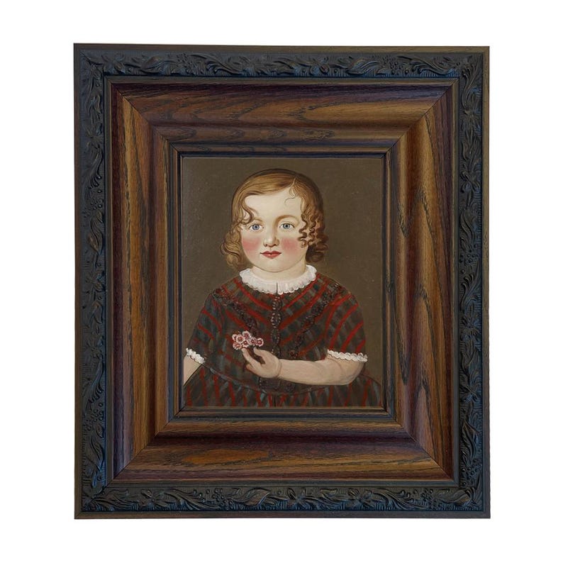 May include: A framed portrait of a child with curly hair, wearing a red and black plaid dress. The child is holding a small flower. The frame is dark brown with ornate detailing.