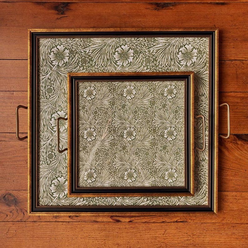 May include: Two decorative trays with floral patterned inserts. The larger tray has a gold frame with brass handles, and the smaller tray has a black frame. The floral pattern features white flowers and green leaves on a cream background.