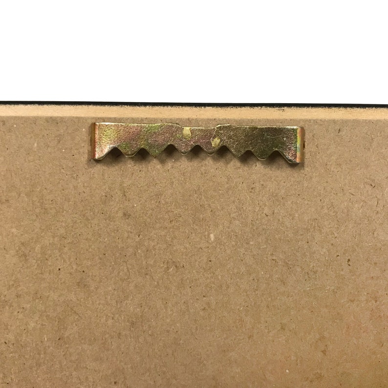 Op de afbeelding: Een close-up van de achterkant van een ingelijst beeld dat een gouden zaagtandhanghaak laat zien.
