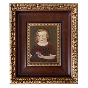 May include: A framed portrait of a young child. The portrait is set within a dark brown frame with a gold ornate outer frame. The child is wearing a red and black patterned dress and holding a small flower.