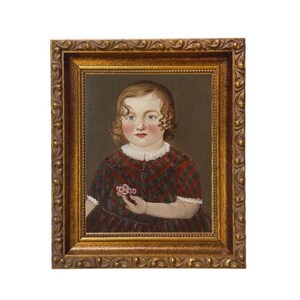 May include: A framed portrait of a young child. The child has curly brown hair, rosy cheeks, and is wearing a red and black plaid dress with a white collar. The child is holding a small pink flower. The frame is gold.