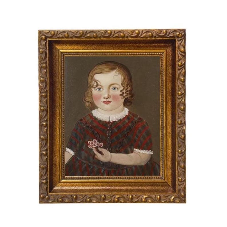 May include: A framed portrait of a young child. The child has curly brown hair, rosy cheeks, and is wearing a red and black plaid dress with a white collar. The child is holding a small pink flower. The frame is gold.