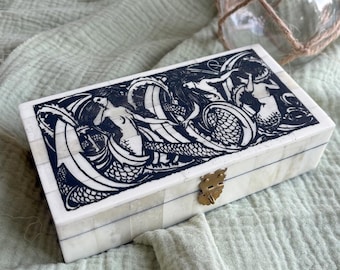 May include: A rectangular box with a white tiled surface featuring a black ink illustration of mermaids swimming among waves on the lid. The box has a brass-colored metal latch on the front and is constructed from small, joined rectangular pieces.