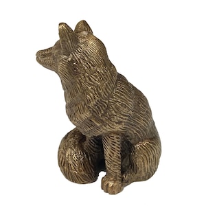 May include: A small, gold-colored metal sculpture of a fox sitting with its head tilted up. The fox is detailed with fur texture.