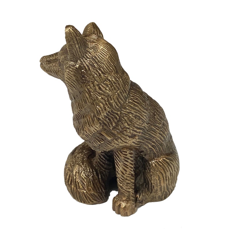 May include: A small, gold-colored metal sculpture of a fox sitting with its head tilted up. The fox is detailed with fur texture.