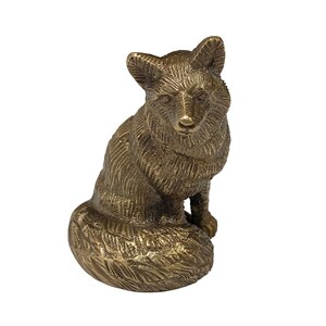 May include: A gold-colored metal figurine of a fox sitting with its tail curled around its body. The fox has a detailed, textured surface.