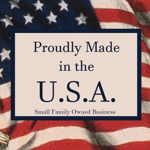 May include: A rectangular sign with the text "Proudly Made in the U.S.A." in navy blue font, set against a cream background. The sign is framed by a navy blue border and is superimposed on an American flag.