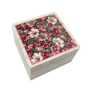 May include: A square decorative box with a floral design on the lid. The lid features a pattern of white, pink, and burgundy flowers on a dark background. The box has a cream-colored frame and sides.