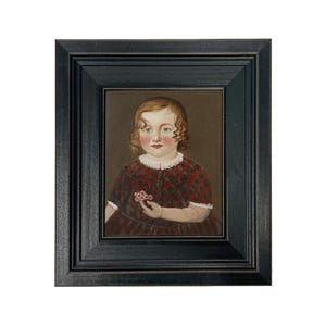 May include: A framed portrait of a young child with curly hair, wearing a red and black plaid dress. The child is holding a small flower. The frame is black.