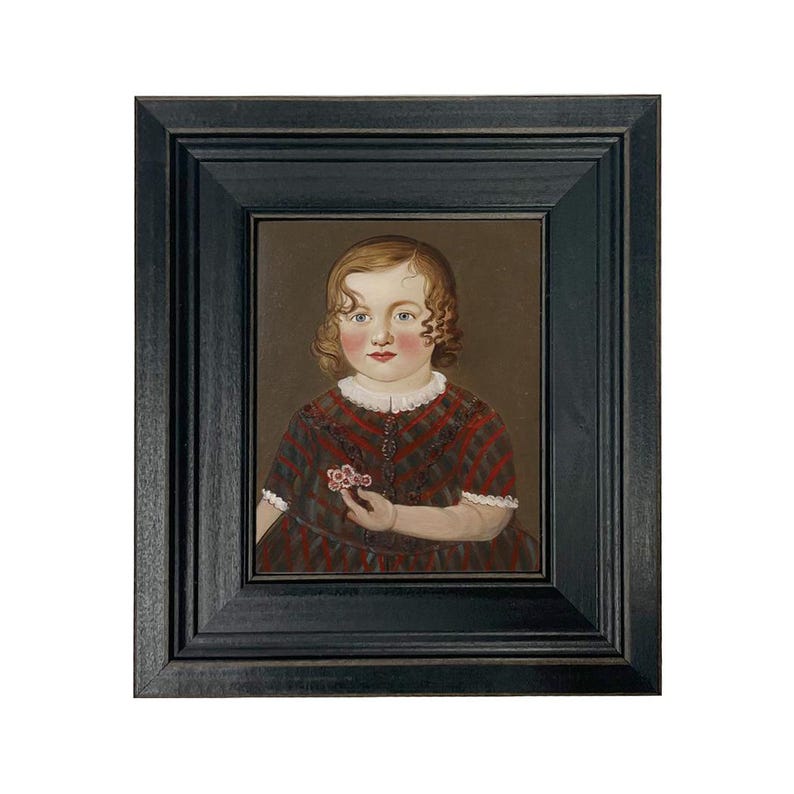 May include: A framed portrait of a young child with curly hair, wearing a red and black plaid dress. The child is holding a small flower. The frame is black.
