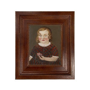 May include: A framed portrait of a young child. The child has curly blonde hair, rosy cheeks, and is wearing a red, black, and white patterned dress. The child is holding a small flower. The frame is a dark brown color.