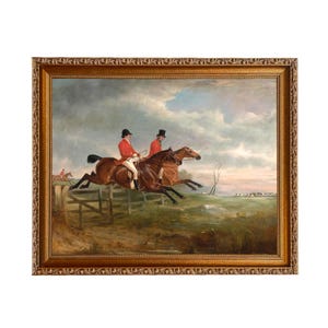 Puede incluir: Pintura antigua enmarcada que representa a dos jinetes a caballo saltando una valla, con un tercer jinete al fondo. Los jinetes visten abrigos rojos y sombreros negros. La pintura tiene un marco dorado.