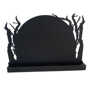 May include: Black silhouette of a moon with branches and leaves around it. The moon is on a black stand.