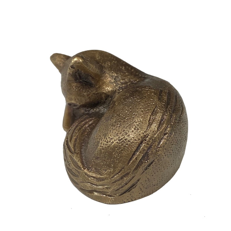 May include: A small, curled-up bronze fox figurine. The fox is depicted in a sleeping position with its tail wrapped around its body.