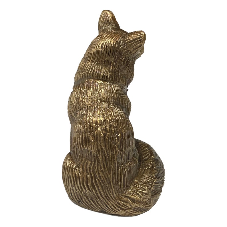 May include: A gold-colored metal figurine of a fox sitting with its tail curled around its body. The figurine is detailed with fur texture and has a realistic appearance.