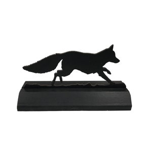 May include: Black wooden silhouette of a fox running, mounted on a black wooden base.