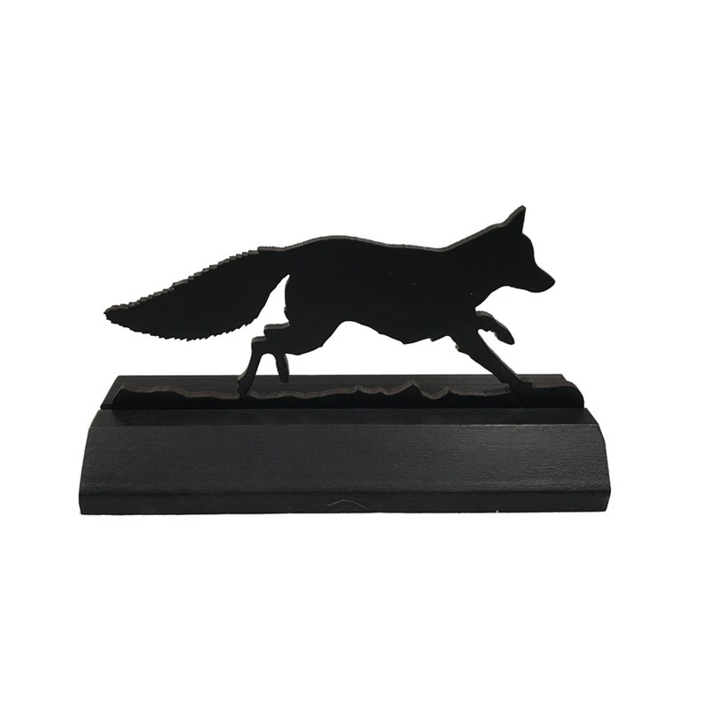 May include: Black wooden silhouette of a fox running, mounted on a black wooden base.