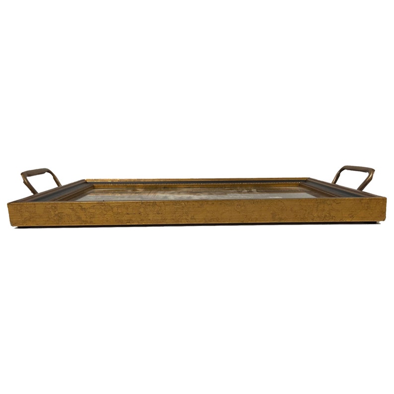 May include: A gold-colored serving tray with a dark wood frame and two brass handles. The tray has a distressed finish.