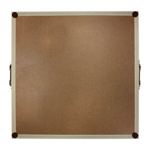 May include: A light brown corkboard with a white frame and rounded corners. The frame has a decorative metal trim and four metal corner accents. The corkboard has two metal handles on the sides.