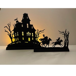 May include: Black silhouette of a haunted house with glowing windows, two figures on horseback riding away from the house, and trees in the background.