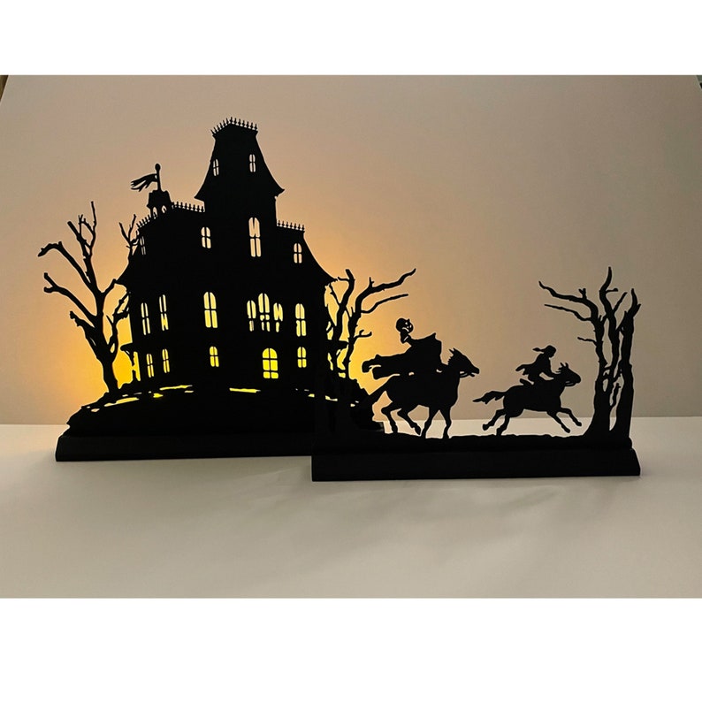 May include: Black silhouette of a haunted house with glowing windows, two figures on horseback riding away from the house, and trees in the background.