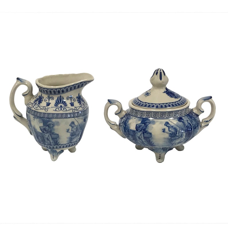 May include: A blue and white porcelain creamer and sugar bowl set with a floral design and a scene of people in a landscape.