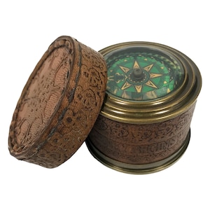 May include: A vintage compass in a leather case. The compass has a green and gold face with a star in the center. The case is brown leather with a floral pattern.