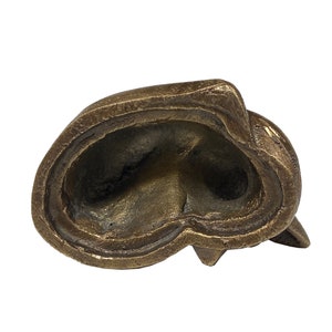 May include: A bronze sculpture of a cat's head, viewed from the bottom. The sculpture is hollow and has a smooth, polished finish.