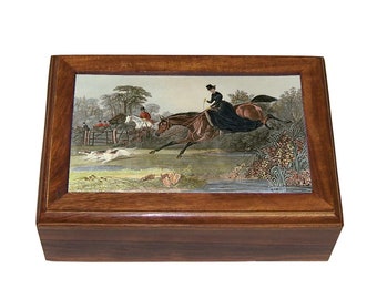 May include: A wooden box with a hinged lid. The lid features a colorful illustration of a woman on horseback jumping over a fence, with other riders and hounds in the background.