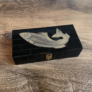 May include: A black wooden box with a gold fish design on the lid. The box has a brass latch.