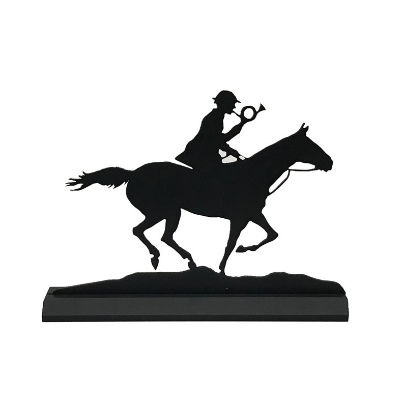 May include: Black metal silhouette of a rider on horseback blowing a horn. The silhouette is mounted on a black base.