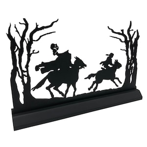 May include: Black silhouette of two figures on horseback riding through a forest. The figures are in the foreground and the trees are in the background. The silhouette is mounted on a black base.