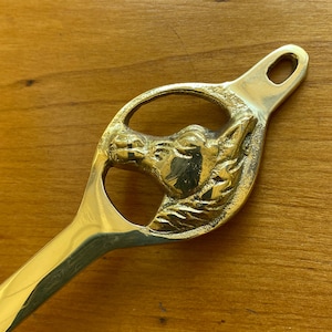 May include: A gold-toned metal horse head doorstop with a detailed design. The horse head is in a circular cutout and the doorstop has a long handle.
