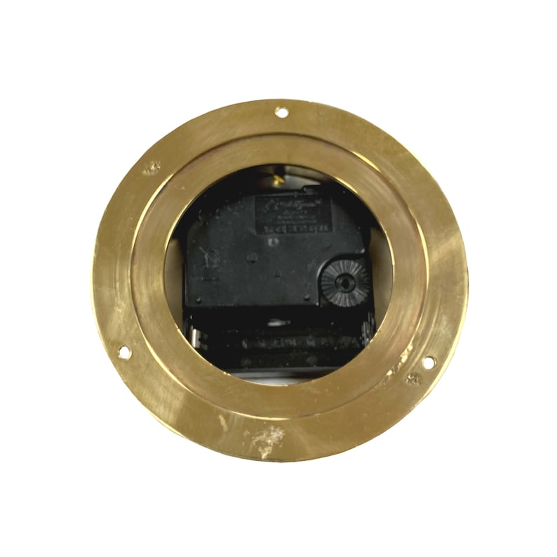 May include: A gold-colored clock mechanism with a black clock face and a silver knob. The clock mechanism is mounted on a round, brass-colored plate with a raised edge.
