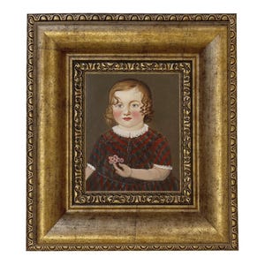May include: A framed portrait of a young child. The child is wearing a red and black plaid dress and holding a small flower. The frame is gold with ornate detailing.