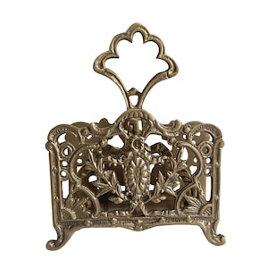 May include: Ornate brass letter holder with a decorative floral and insect design. The vintage desk organizer features a filigree pattern and a curved handle at the top. The brass has a warm, aged patina.