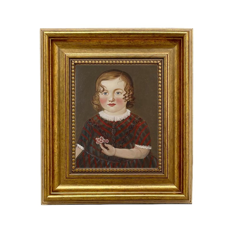 May include: A framed portrait of a young child. The child is wearing a red and black plaid dress and holding a small flower. The portrait is in a gold-colored frame.