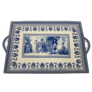May include: A white rectangular serving tray with blue and white floral designs and a central scene of people in a garden. The tray has two handles on the sides.