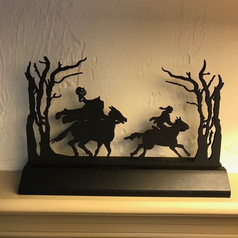 May include: Black metal silhouette wall art depicting three figures on horseback riding through a forest. The figures are silhouetted against a white background.