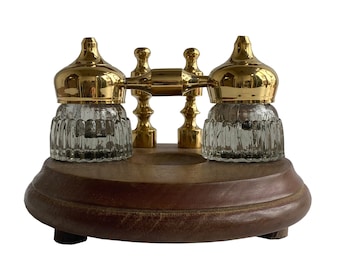 May include: A vintage-style inkwell set with two glass inkwells with gold lids and a brass base. The inkwells are on a wooden base.