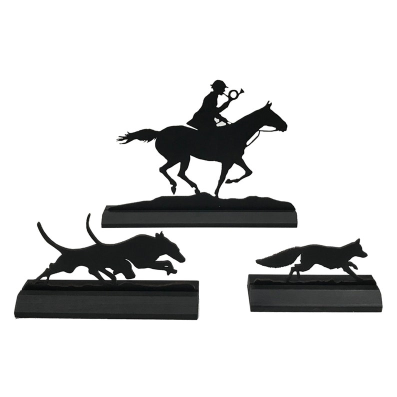 May include: Black metal silhouette set of a rider on horseback, a hound, and a fox. The figures are mounted on black bases.