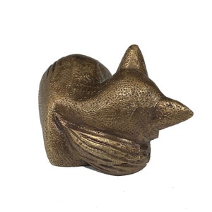 May include: A bronze sculpture of a sleeping fox. The fox is curled up with its tail wrapped around its body. The sculpture is detailed with a textured surface.