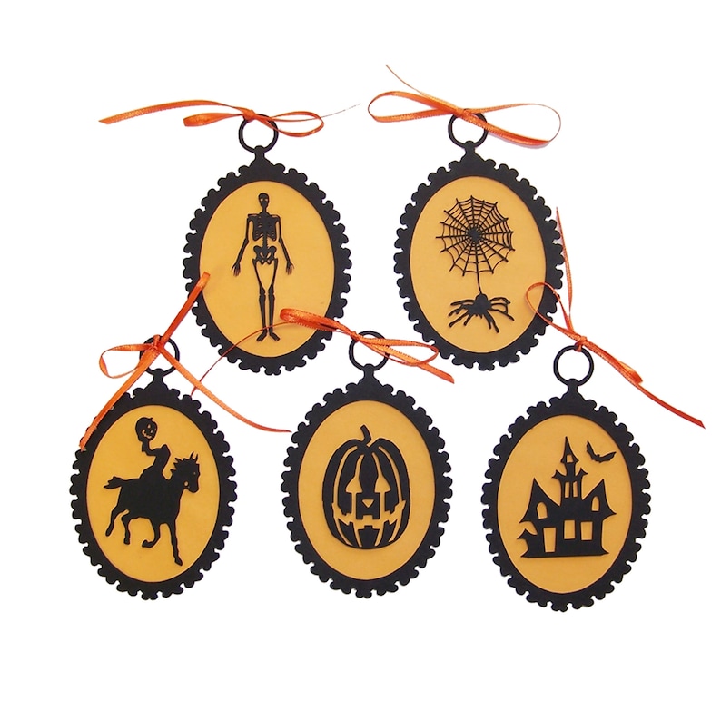 May include: Five black and orange Halloween ornaments with different spooky designs. The ornaments are shaped like ovals with a black scalloped border and a gold background. The designs include a skeleton, a spider web, a pumpkin, a haunted house, and a rider on a horse.