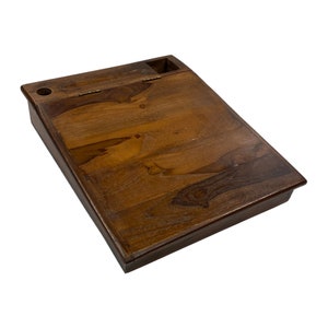 May include: A wooden writing desk with a hinged top and a small compartment. The desk is made of dark brown wood with visible grain patterns. It features a small hole and a rectangular storage area.