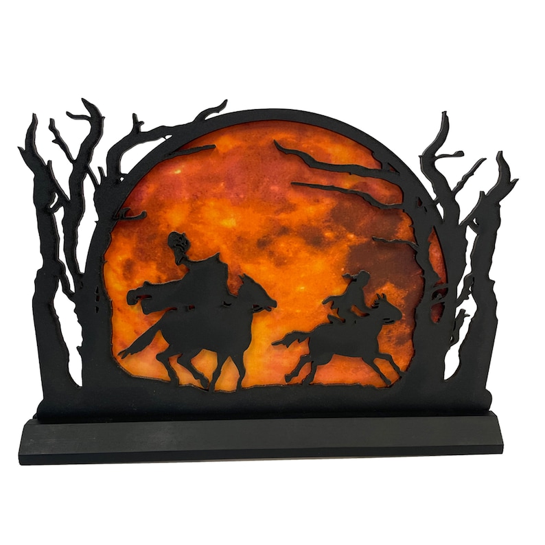 May include: Black silhouette of two figures riding horses against a backdrop of a large orange moon and trees. The moon has a textured, marbled appearance.