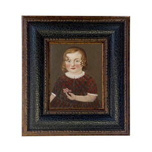 May include: An antique portrait of a young child in a dark wooden frame. The child is wearing a red and black plaid dress and holding a small flower. The frame has a textured black border and a gold inner edge.