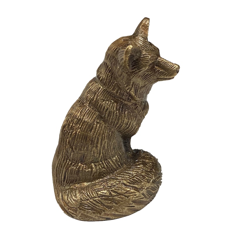 May include: A gold-colored metal figurine of a fox sitting with its tail curled around its body. The fox has a detailed, textured surface.