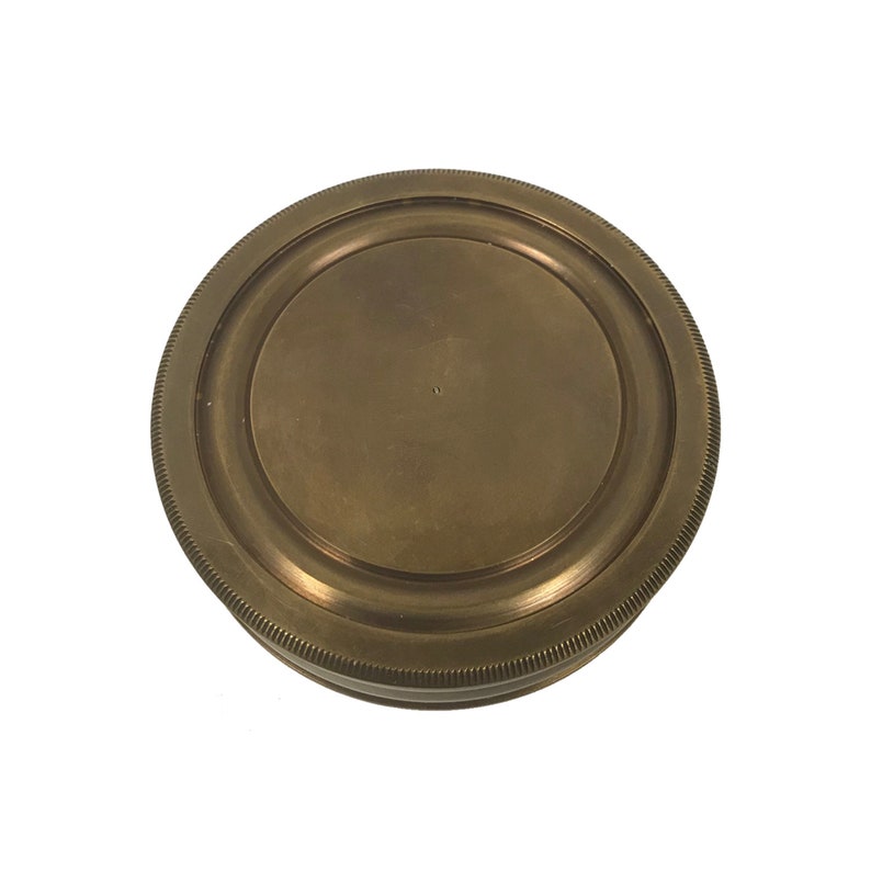 Puede incluir: Un objeto redondo de color lat&oacute;n antiguo, con un borde estriado y un centro circular plano. El objeto tiene una est&eacute;tica vintage y parece estar hecho de metal. El dise&ntilde;o es simple y funcional, lo que sugiere que podr&iacute;a ser una tapa o un elemento decorativo.